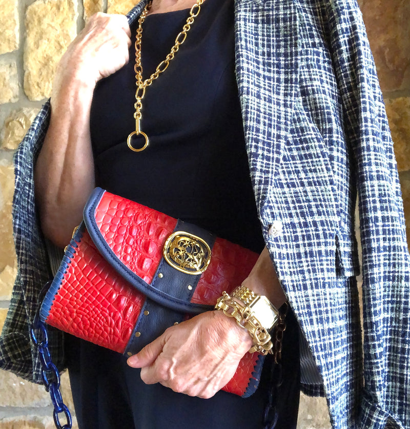 Styled view of red croc print leather bag with navy & gold accents with navy outfit.