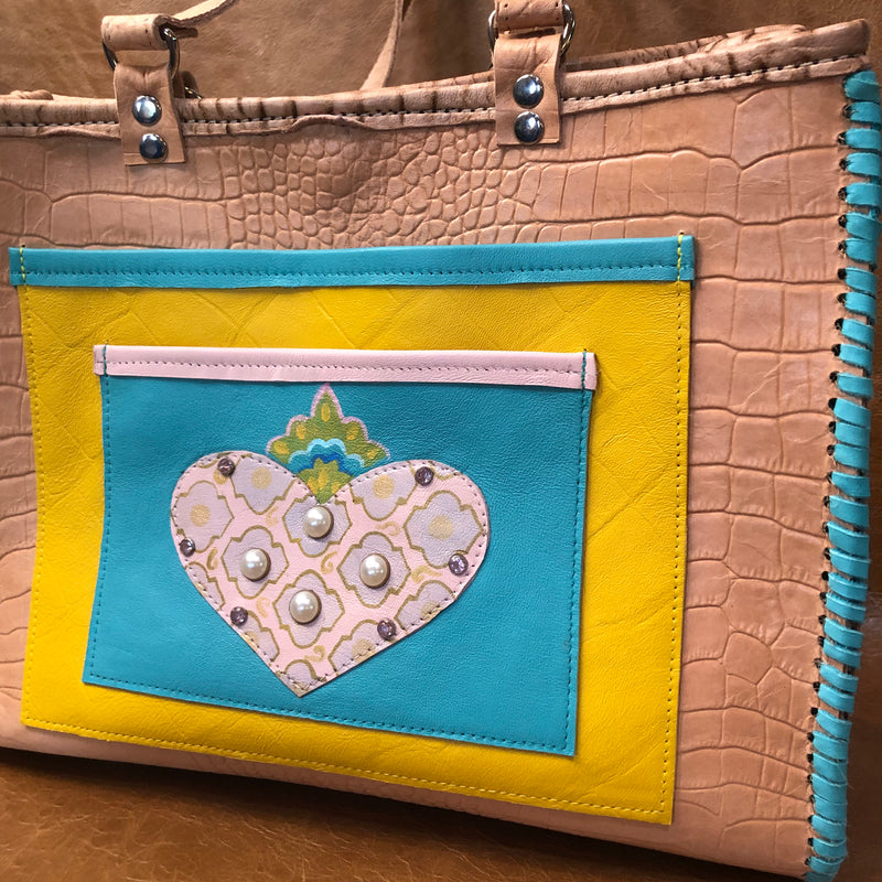 Close up of embellished pocket on front of tan croc print leather tote bag with pink heart applique