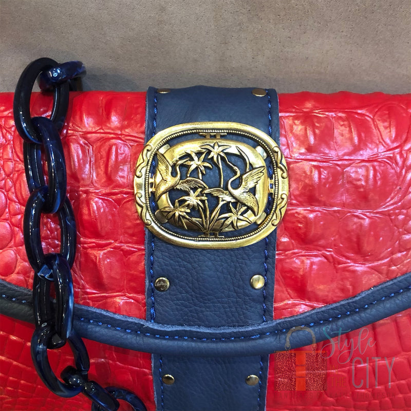 Close up of gold vintage brooch and nailhead accents on red croc print leather bag. 