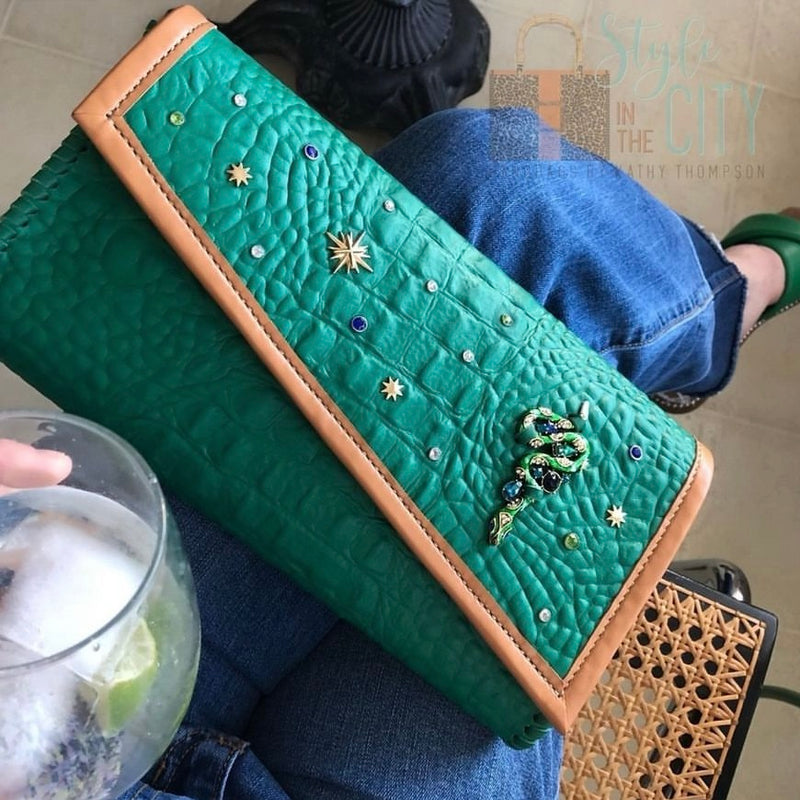 Embellished green croc print leather bag with tan trim shown with denim and green outfit.