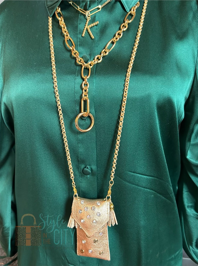 Styled view of gold leather pouch necklace on long gold chain layered with other gold necklaces.