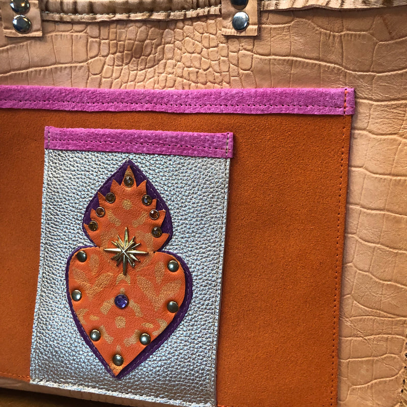Close up of flaming heart embellished front pocket on tan croc print leather tote.