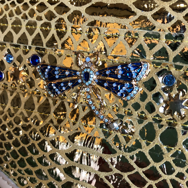 Close up of blue crystal dragonfly on front of gold snake print leather clutch
