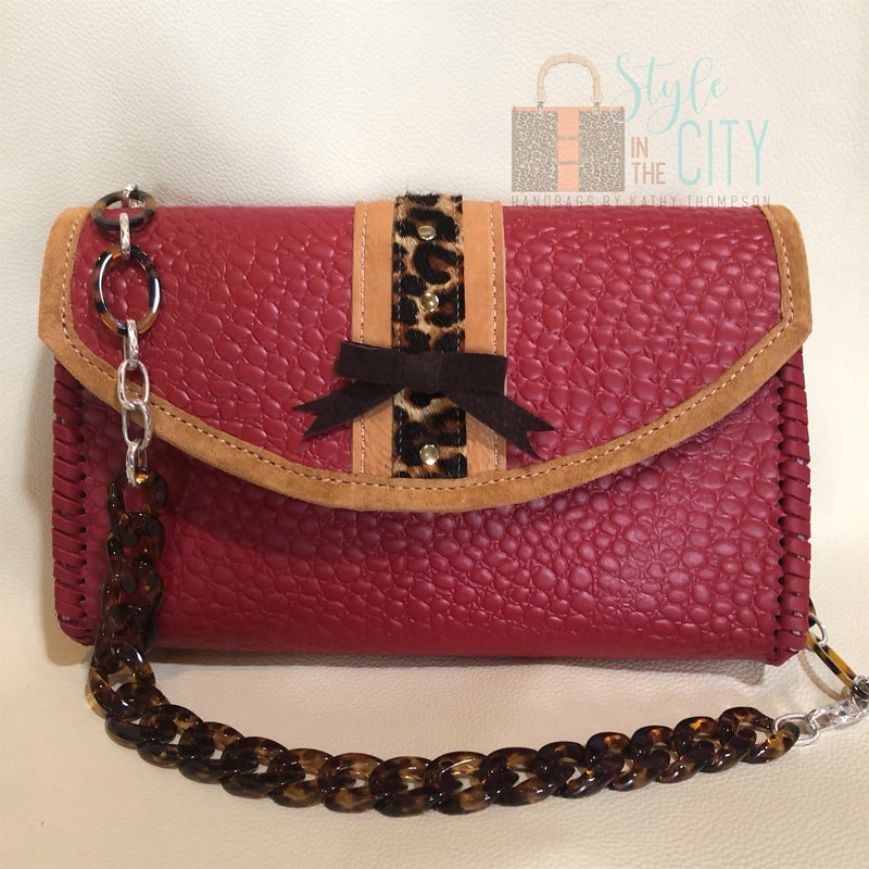 Red leather handbag with leopard trim and acrylic chain handle.