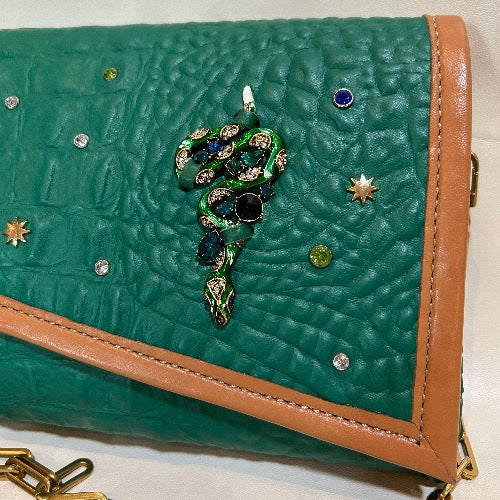 Close up of snake detail on front of green croc print leather bag with tan trim