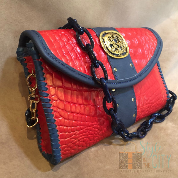 Side view of red croc print leather bag with navy & gold accents.