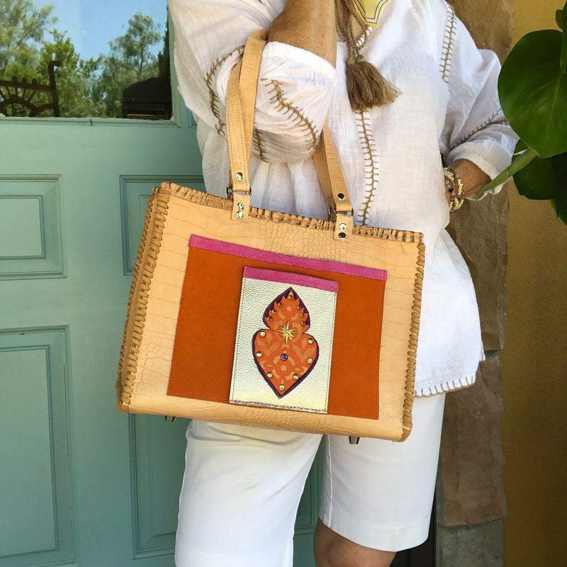 Styled view of tan croc print leather tote bag with flaming heart motif with a white summer outfit. 