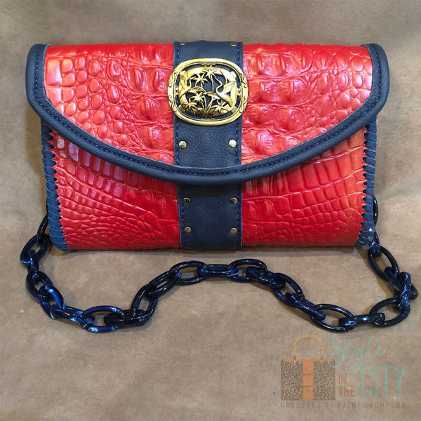 Red croc print leather bag with navy & gold accents and acrylic chain handle.