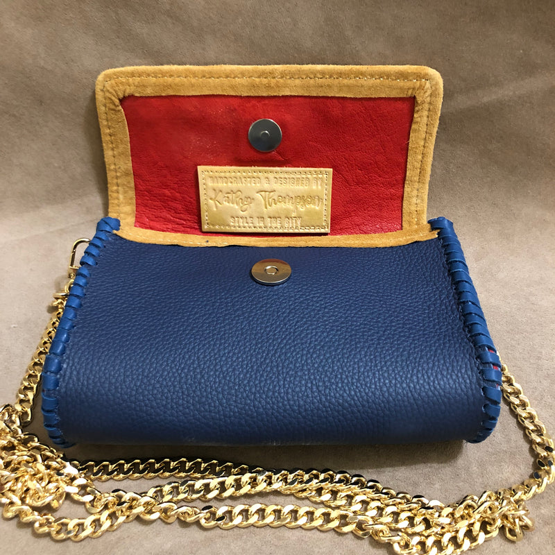 Red leather interior of navy & tan leather mini bag with long gold chain.