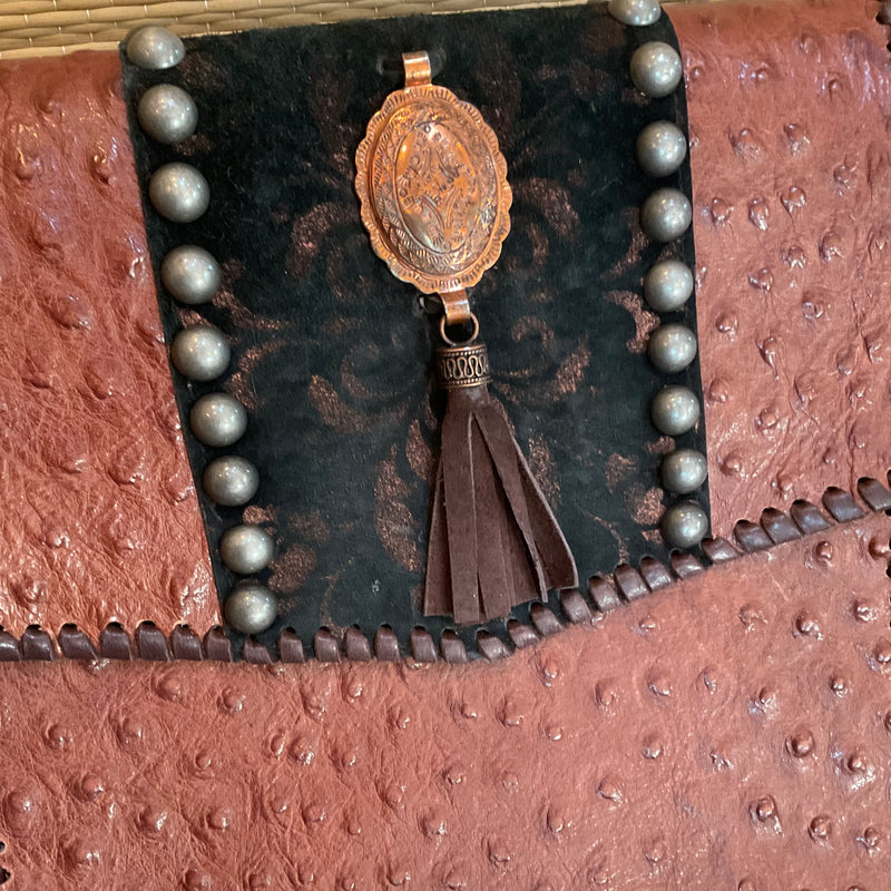 Close up view of concho & domed nailheads & tassel accents on brown ostrich print crossbody. 