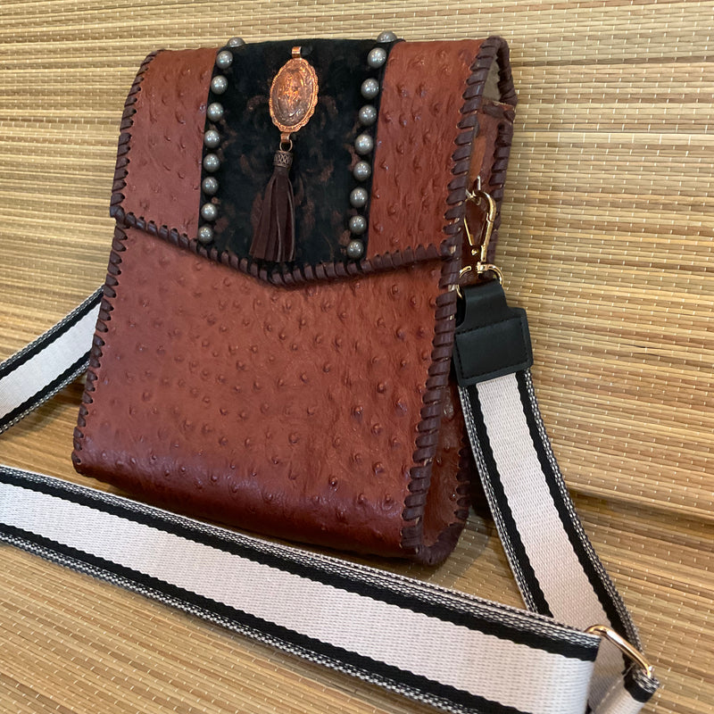 Side angle view of brown ostrich print leather crossbody bag with black & copper accents.