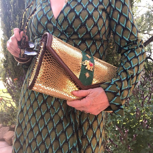 Styled view of gold snake print leather envelope clutch with vintage elephant with green print dress.