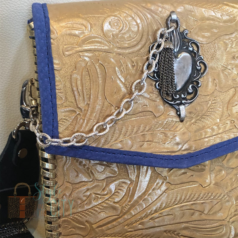 Close up of chain, heart , & tassel accents on front of metallic gold leather crossbody bag with boho strap